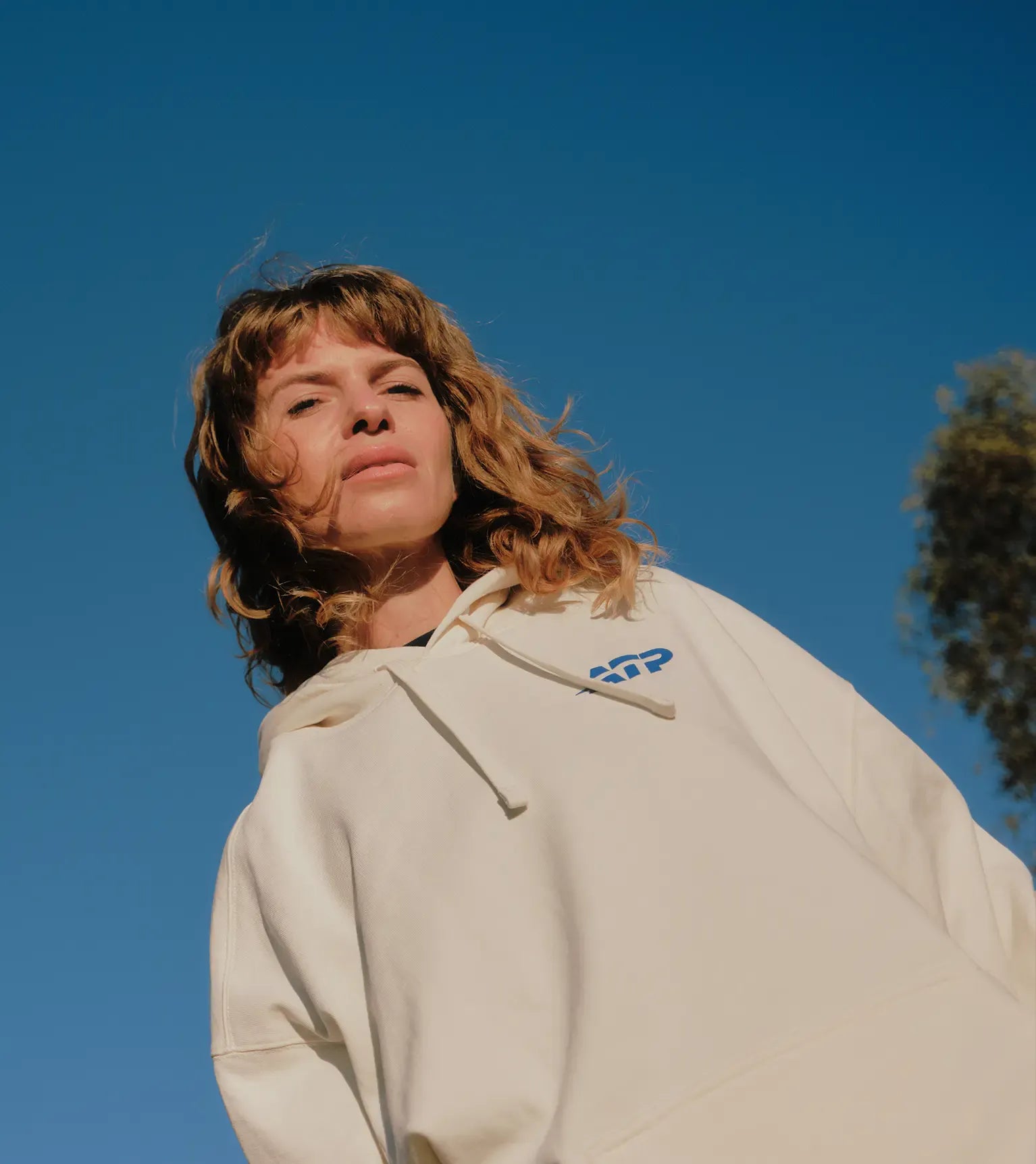 Woman wearing a white ATP hoodie against a clear blue sky