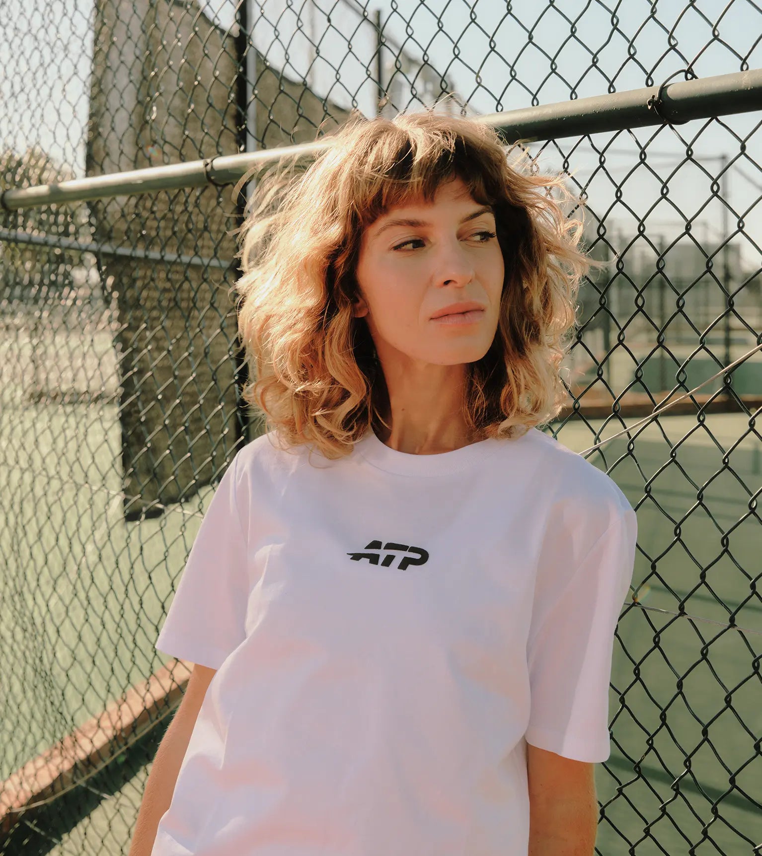 Woman standing in front of a chain-link fence with a tennis court in the background.