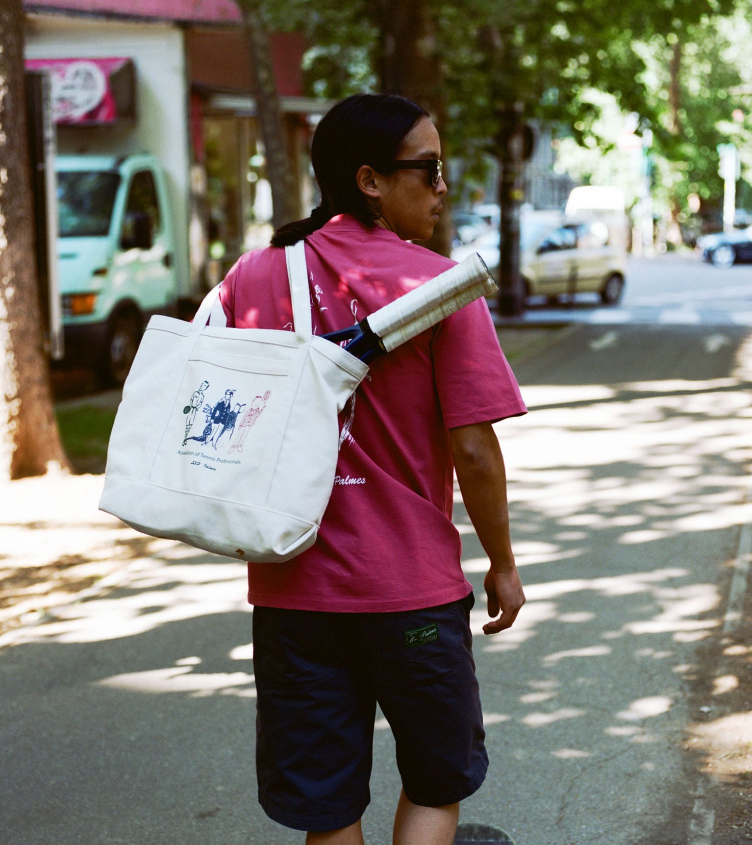 Man walking on the sidewalk holding a tote bag with tennis rackets in the bag